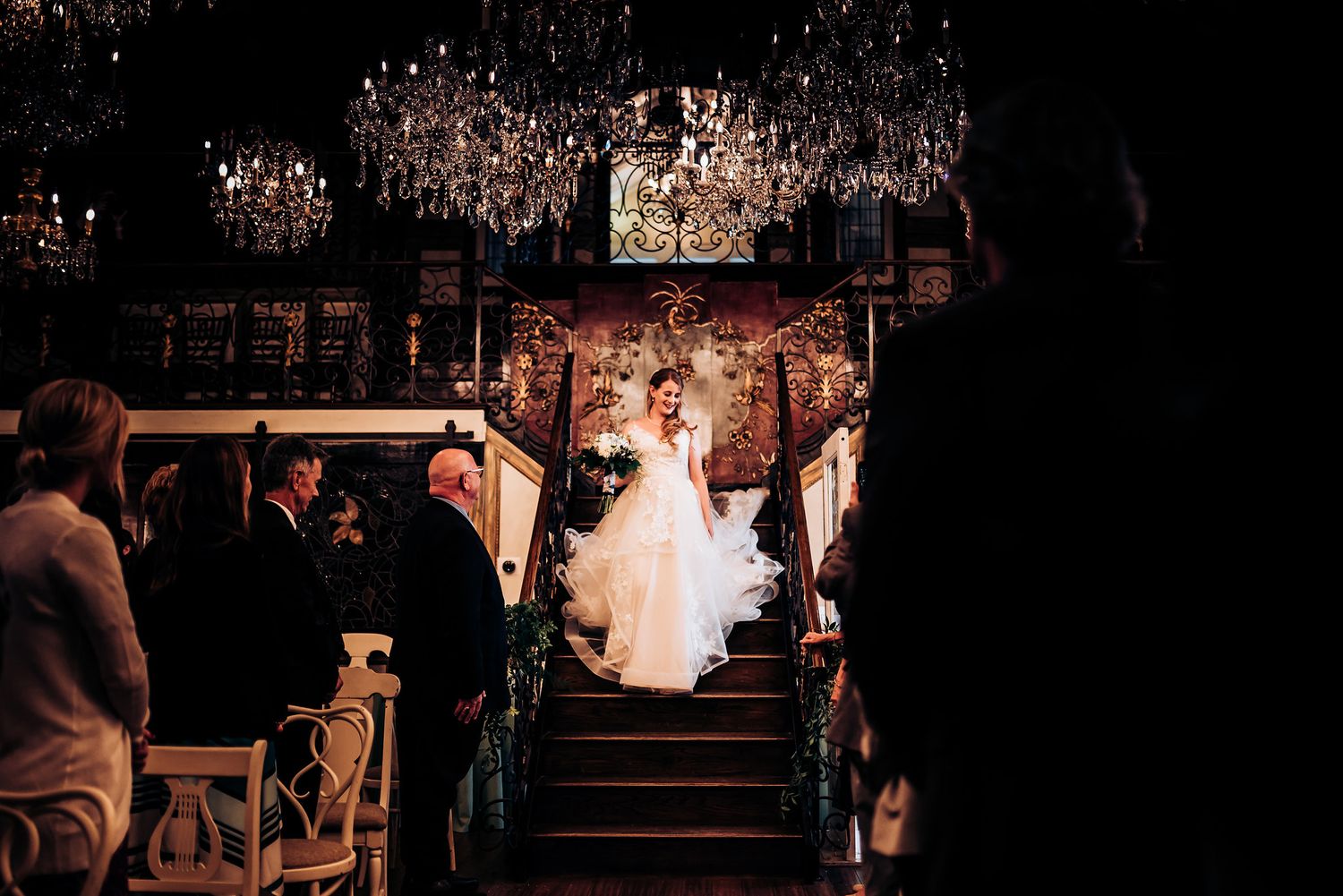 Dramatic wedding ceremony scene with chandeliers illuminating the venue's grand staircase.