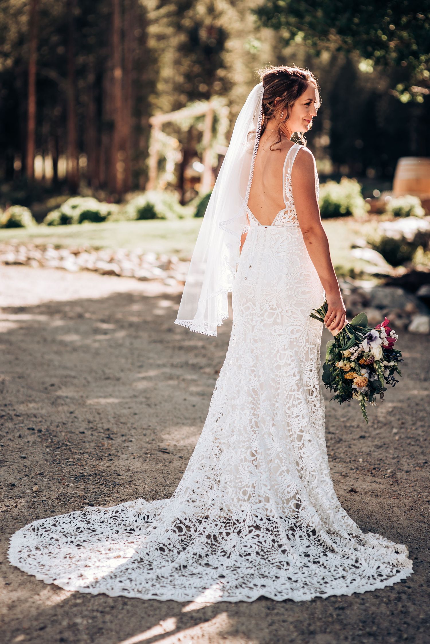 An elegant lace wedding dress with long train photographed in natural outdoor lighting.