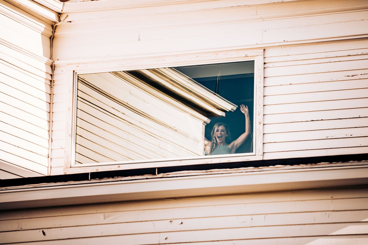 A curious dog peeks through a window in white siding of a house.
