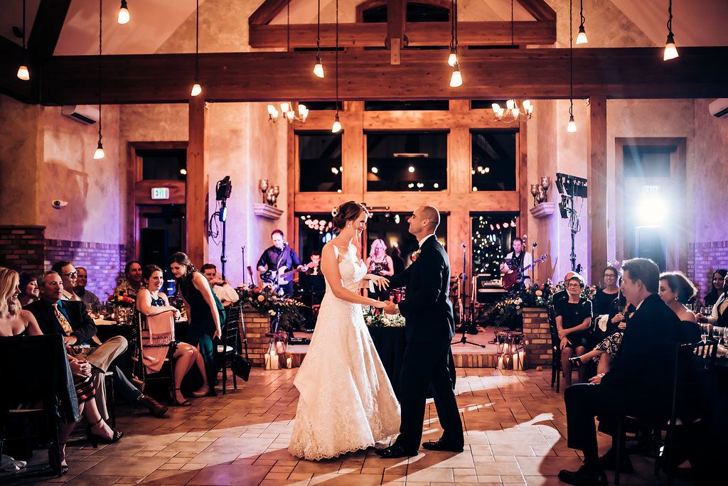 First dance at wedding reception with guests seated around rustic venue with string lights.