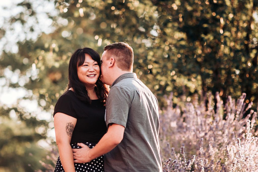Couple embraces in sunlit garden with blooming flowers in background.