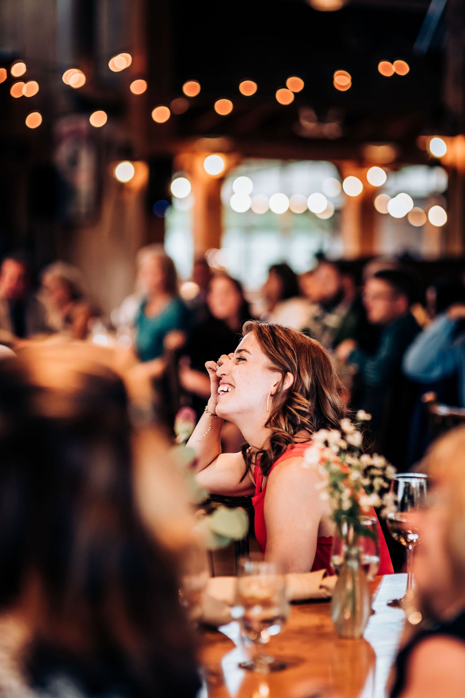 Guest laughing joyfully during reception dinner with bokeh lights in background.