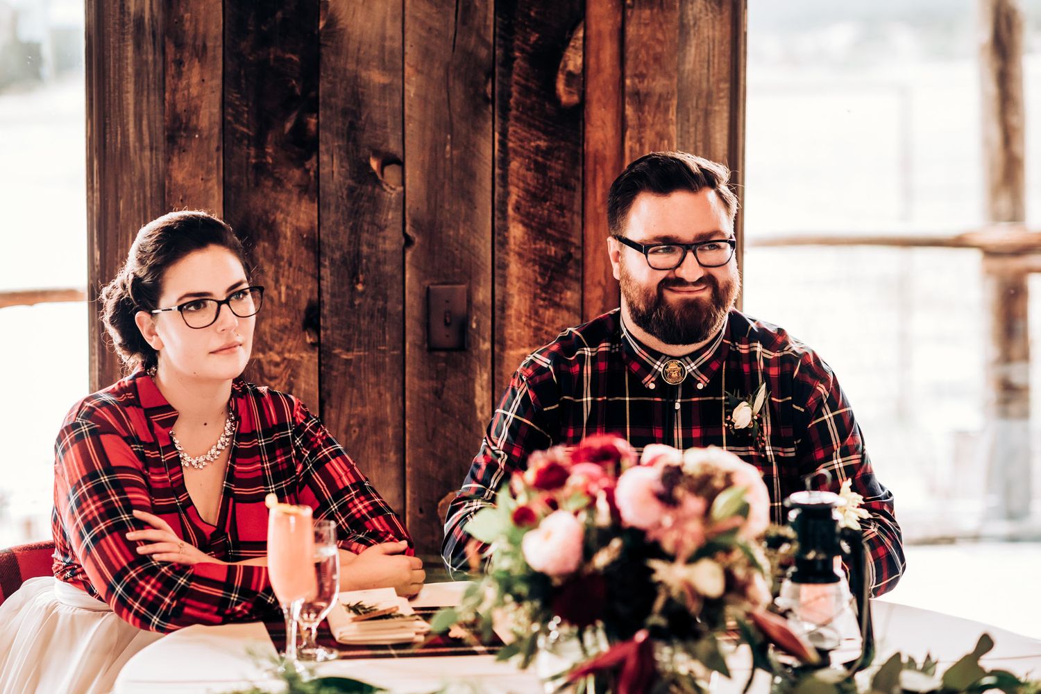 A couple enjoying drinks and food at a rustic wooden table with floral centerpiece.