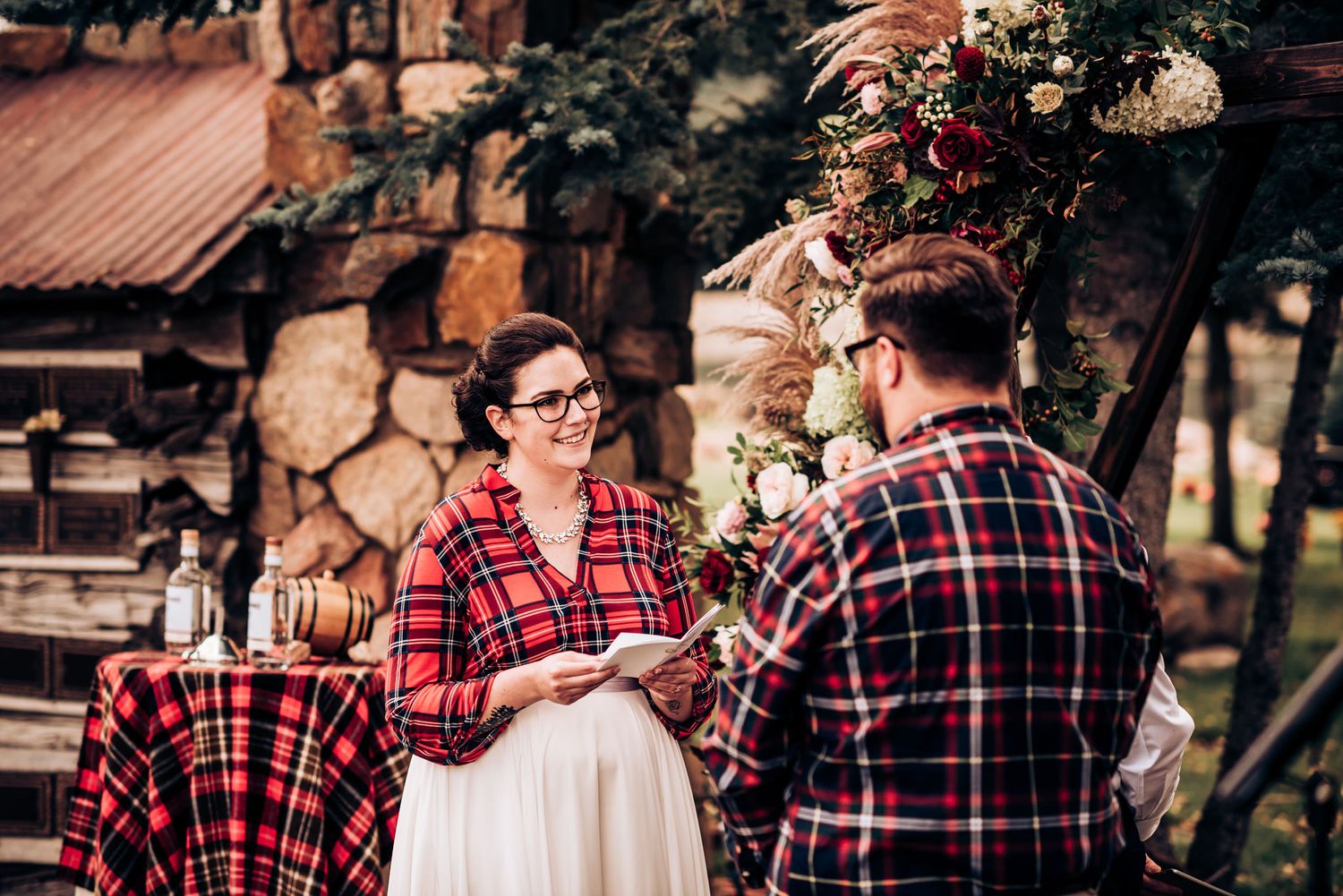A couple exchanges vows beneath a floral arch against a rustic stone and wood backdrop.