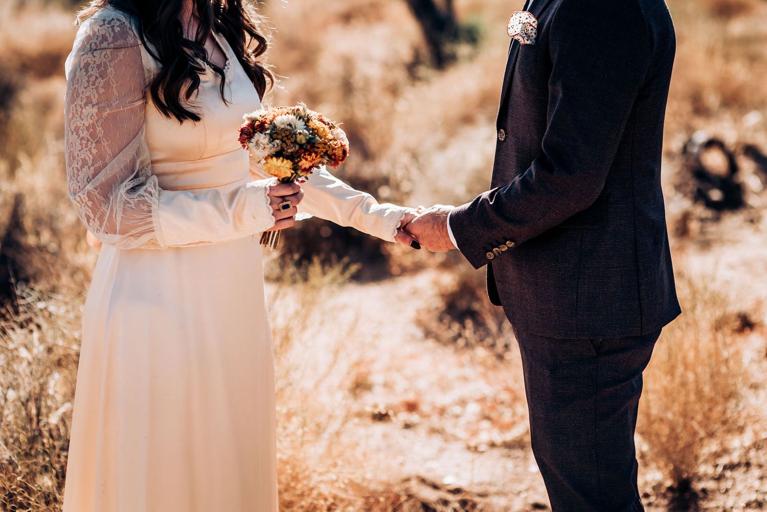 A wedding couple exchanges rings in a rustic desert setting.