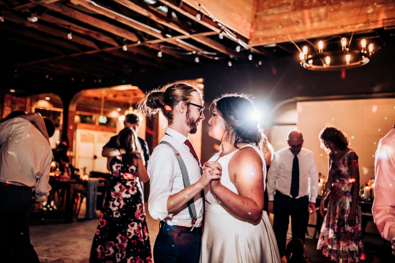 Dancing couples enjoy a romantic moment during wedding reception in rustic indoor venue.