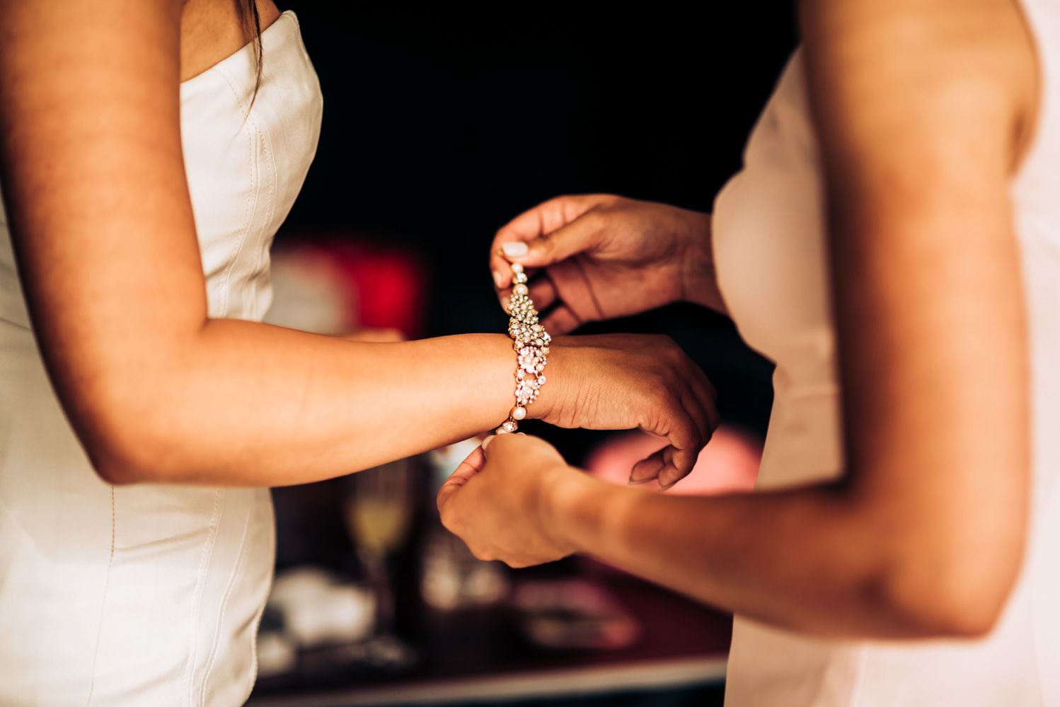 Close-up of hands fastening a bracelet or jewelry piece against white formal attire.