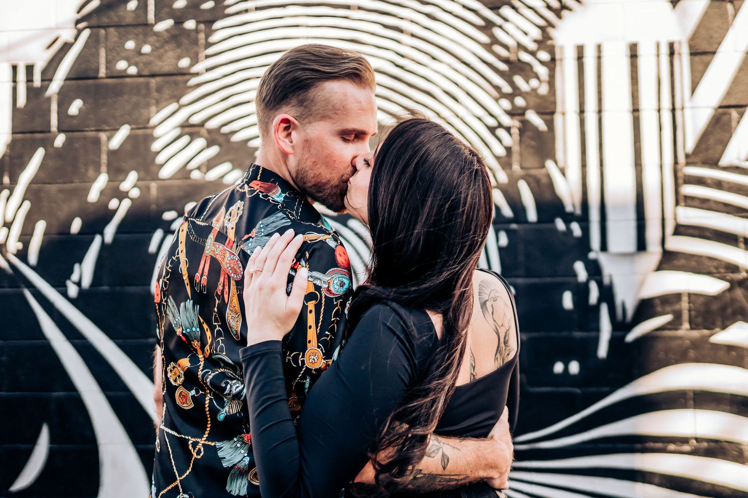 A couple embracing in front of a geometric black and white street art mural.