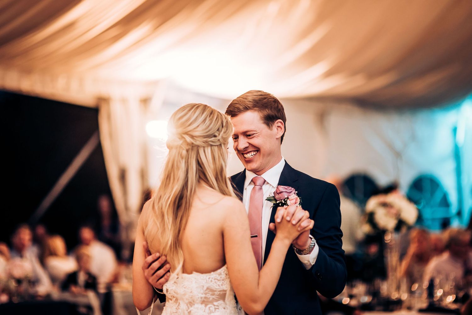 Couple sharing a dance moment under warm reception lighting with draped tent ceiling.