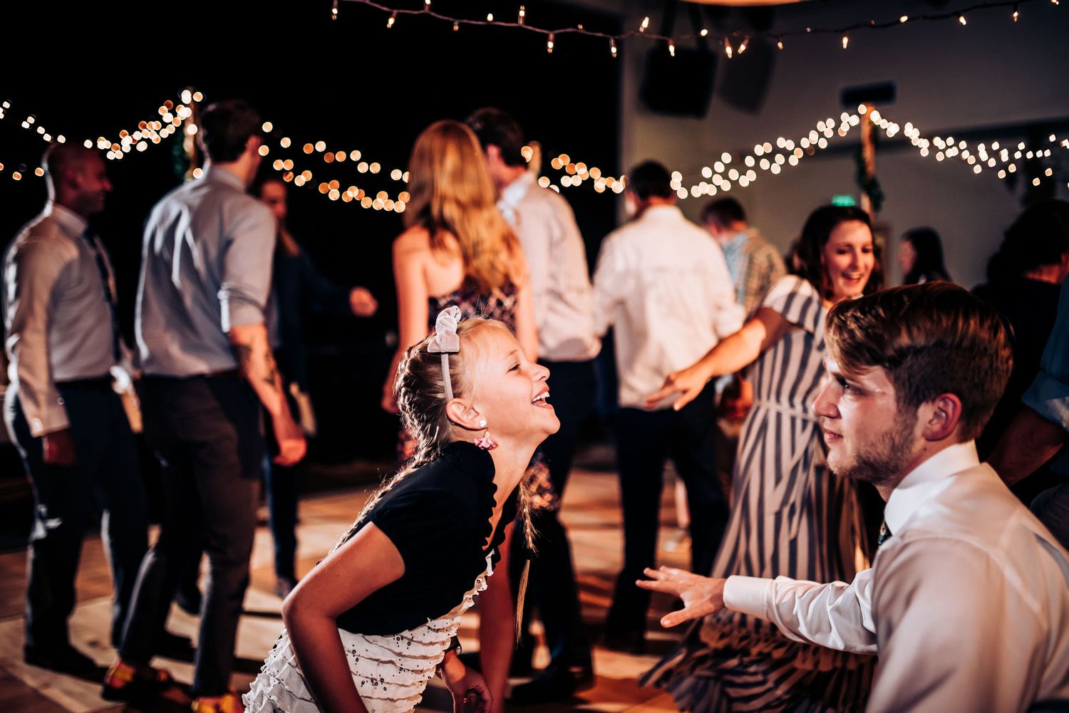 Lively wedding reception dance floor with string lights creating festive atmosphere.