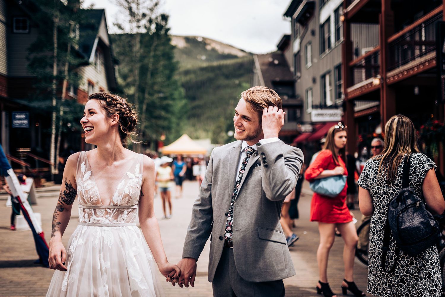 Newlyweds walk hand in hand through mountain town street during wedding celebration.