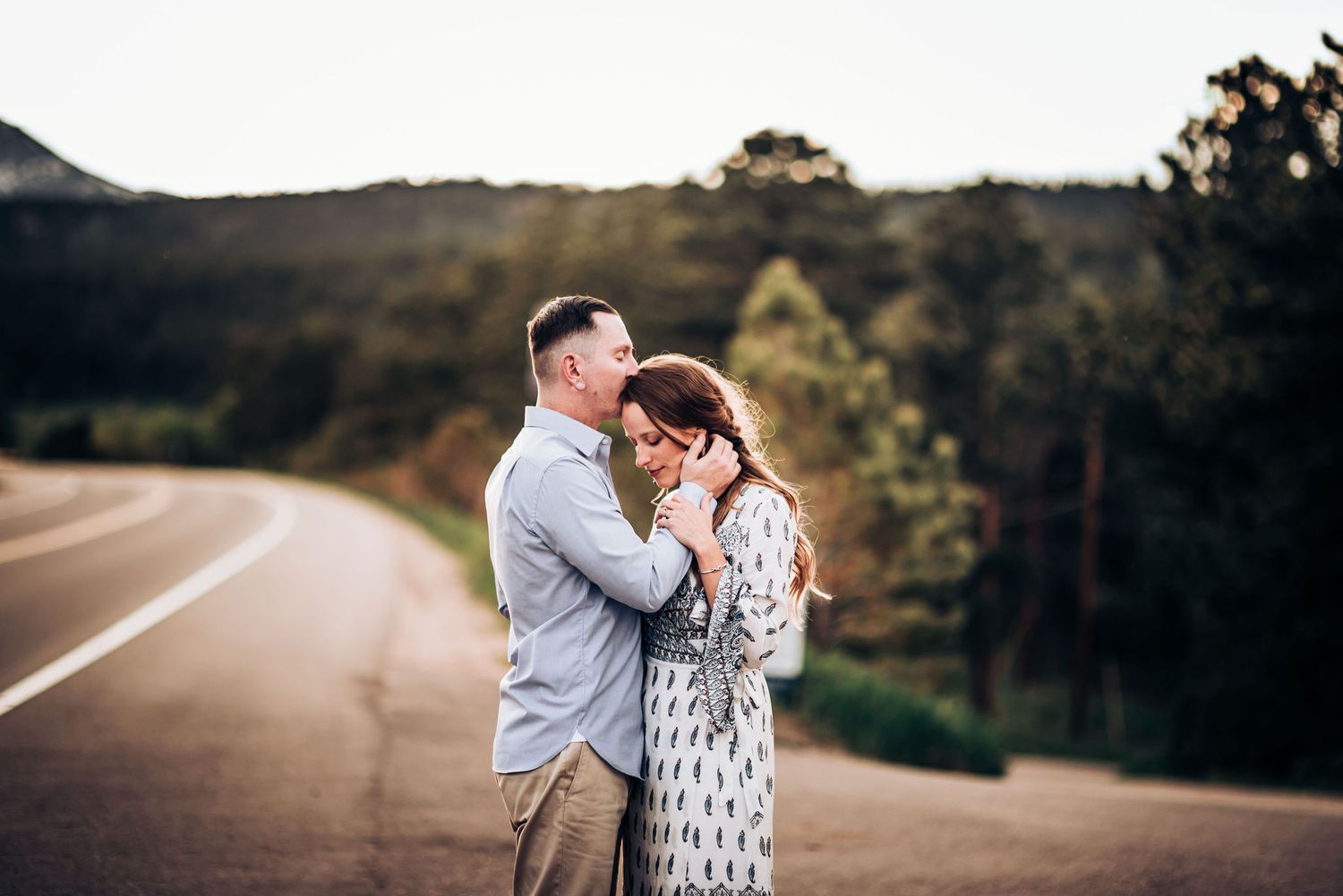 A couple embraces on a winding mountain road during golden hour photography session.