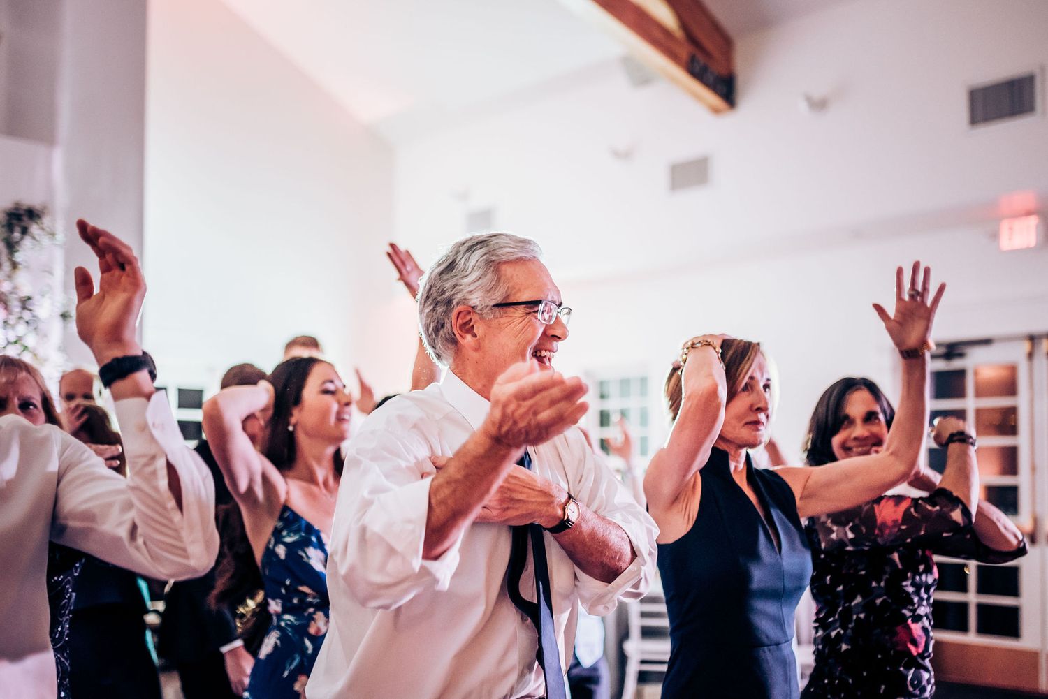 Joyful wedding guests dancing and celebrating with hands in the air during reception.