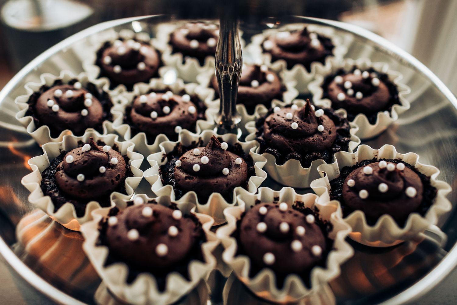Chocolate cupcakes with white sprinkles arranged on tiered serving plate.