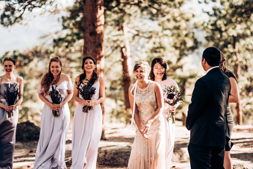 Wedding party stands in formation during an outdoor ceremony among tall pine trees.