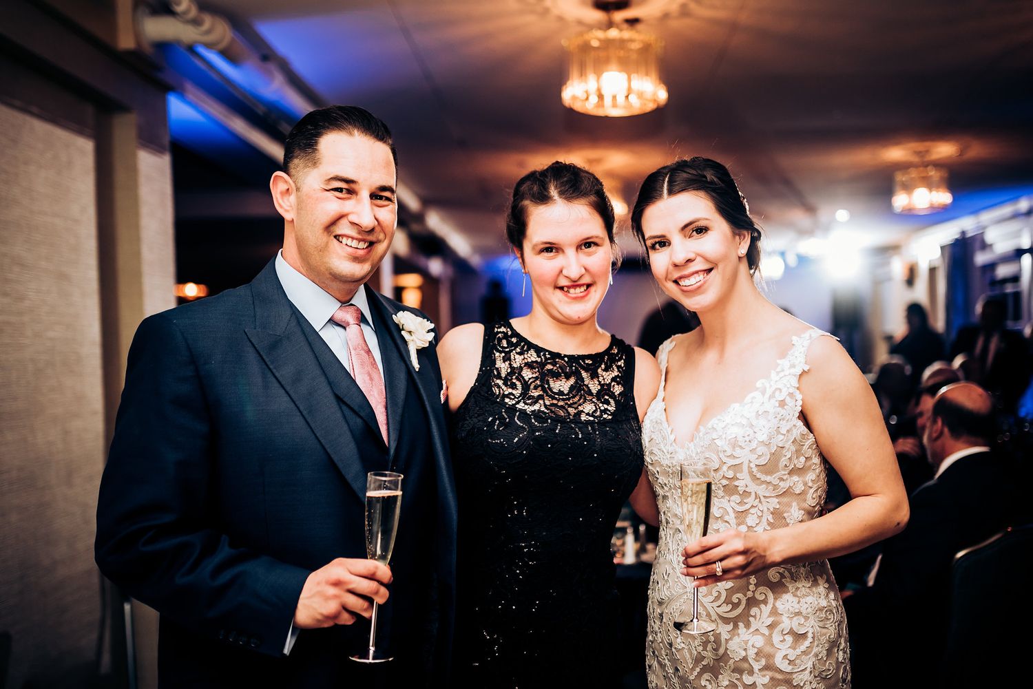 Three guests pose together at an elegant evening wedding reception with champagne glasses.