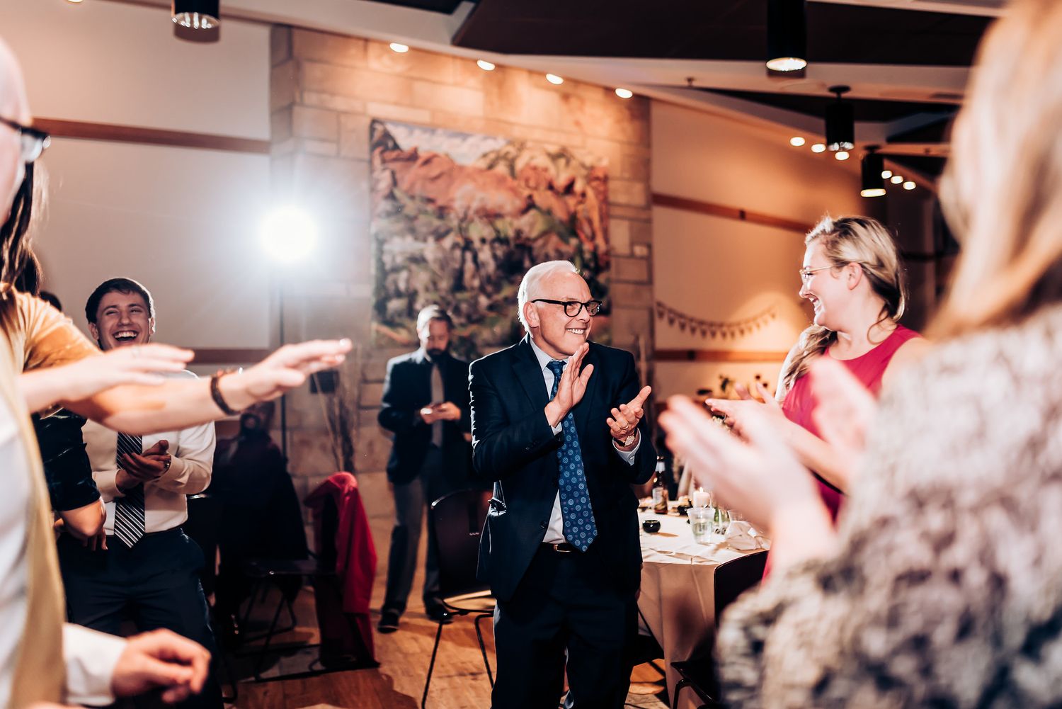 Reception guests dancing and clapping in a venue with decorative wall murals.