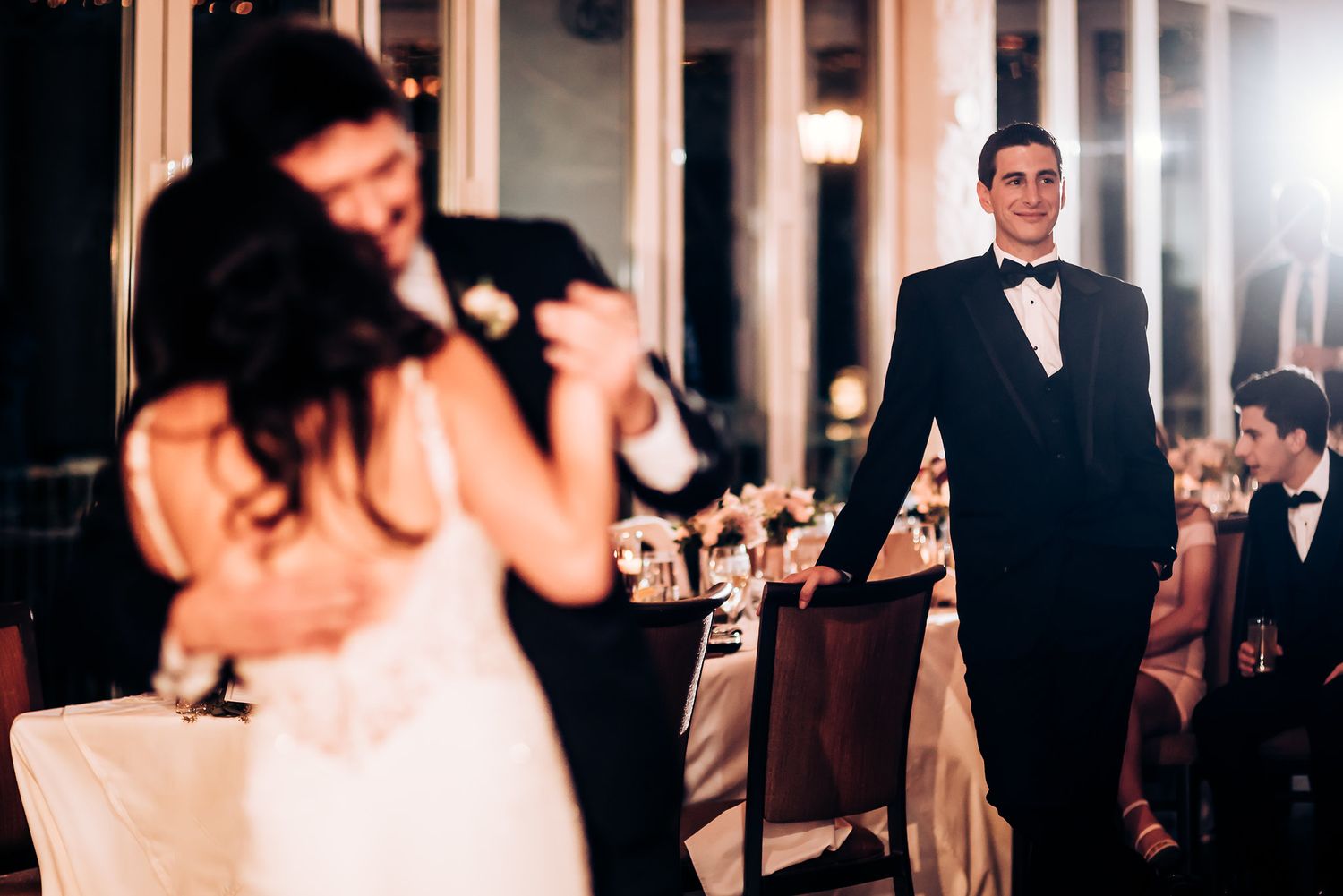 Elegant wedding reception scene with guests in formal attire under indoor lighting.