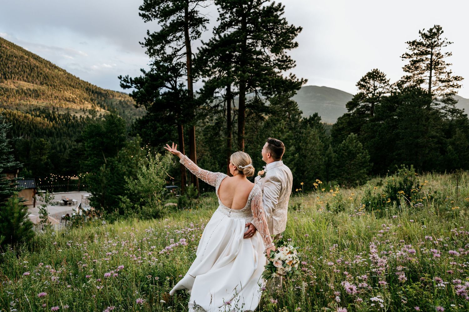 A couple shares a romantic moment in a mountain meadow with wildflowers and evergreen trees.