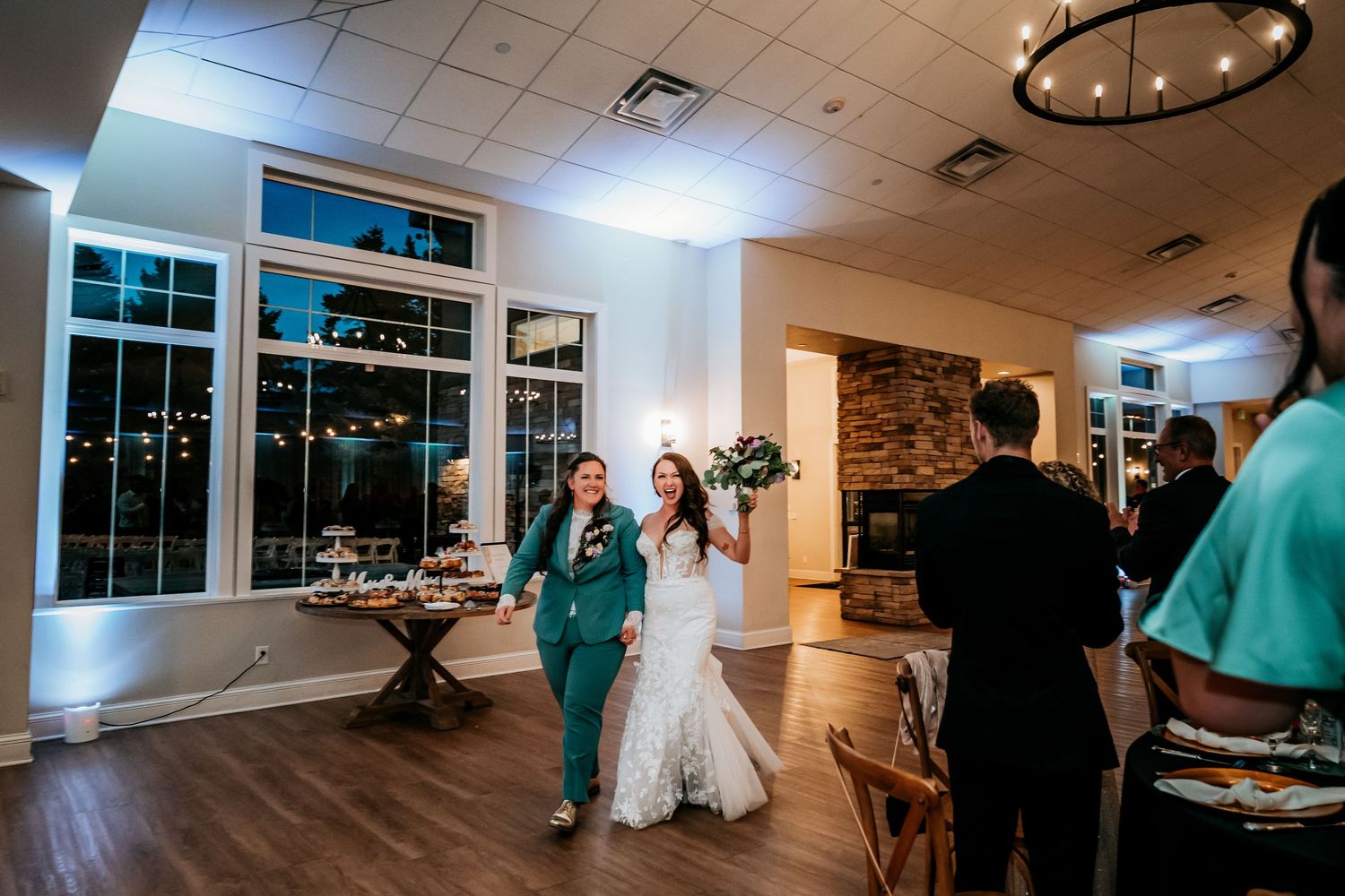 Two brides make a grand entrance into their wedding reception hall hand-in-hand.