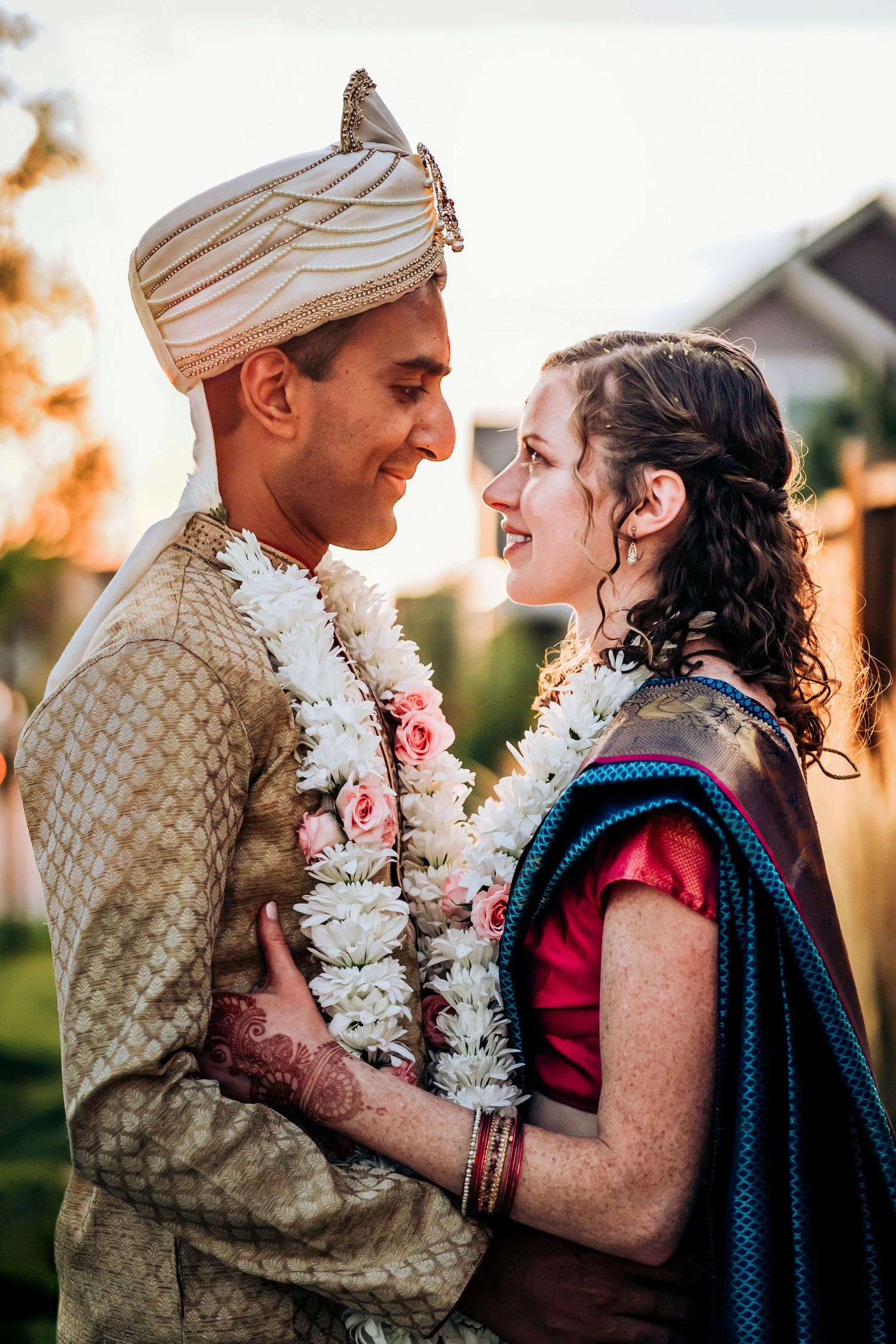 A couple wearing traditional Indian wedding attire shares a joyful moment at sunset.
