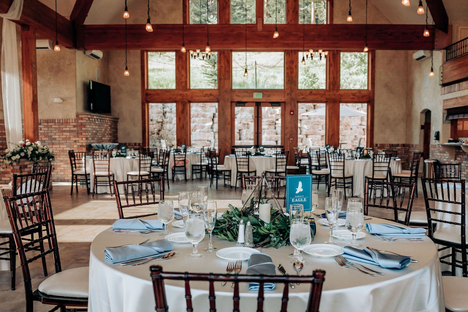A beautifully decorated wedding reception hall with round tables and wooden chairs.