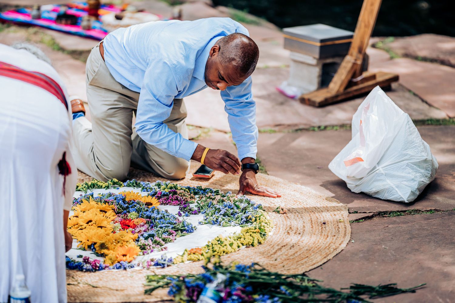 Someone arranges a vibrant floral installation on a wooden surface outdoors.