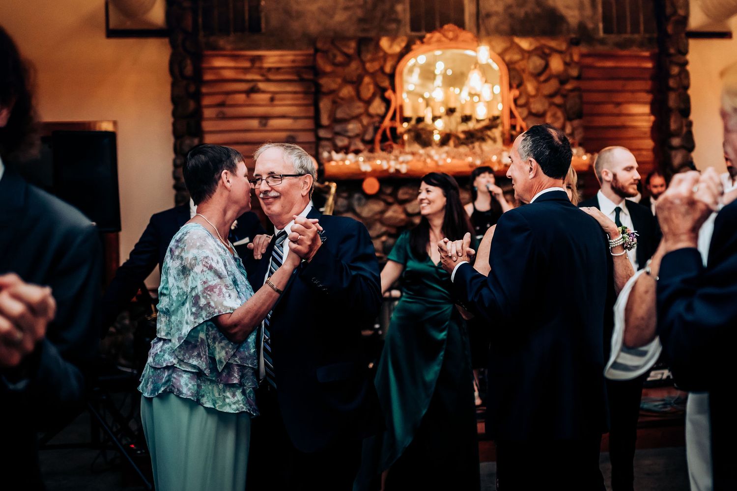 Guests dancing and celebrating at an elegant wedding reception with a warm fireplace in the background.