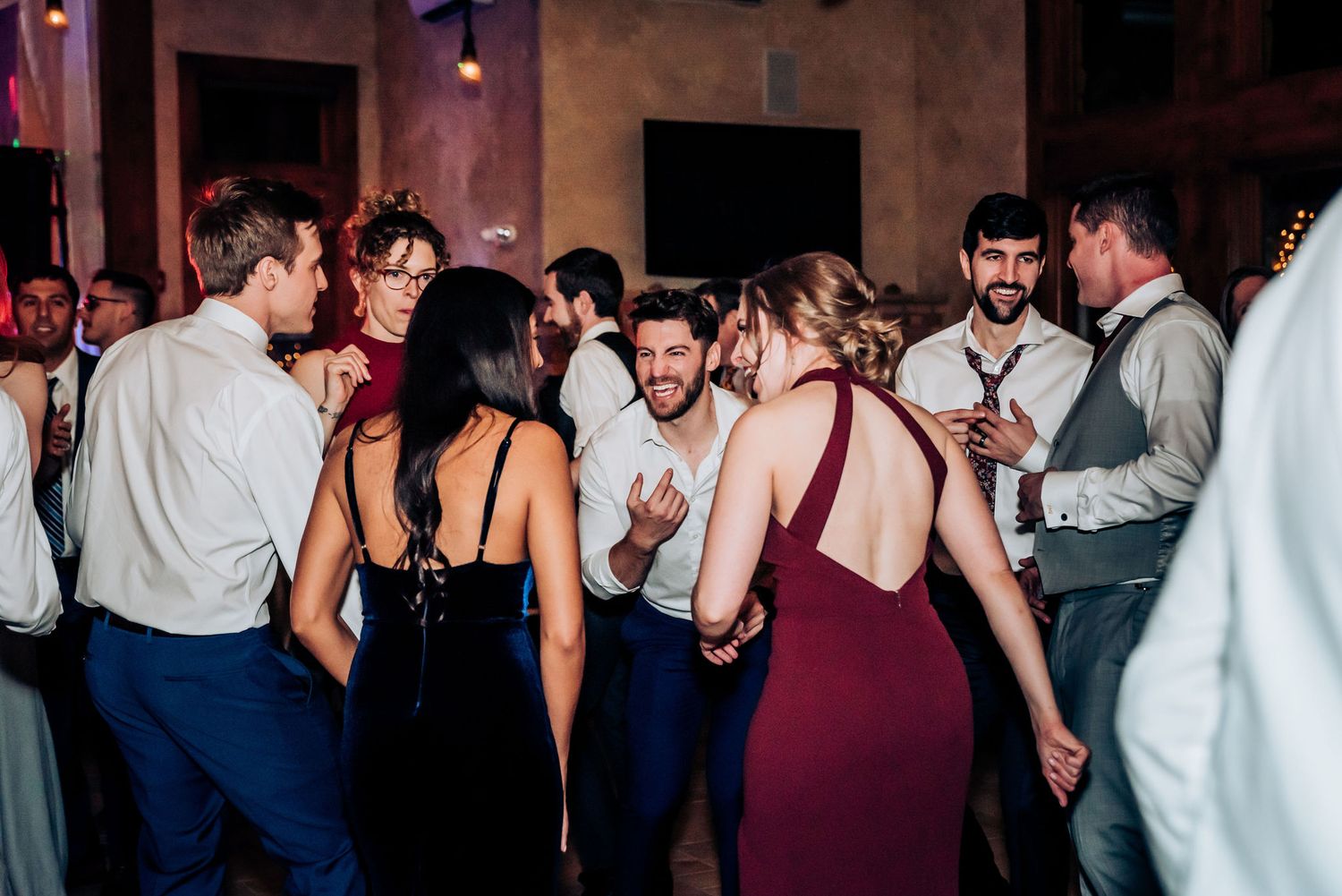 Wedding guests mingling and dancing at an indoor reception with mood lighting.