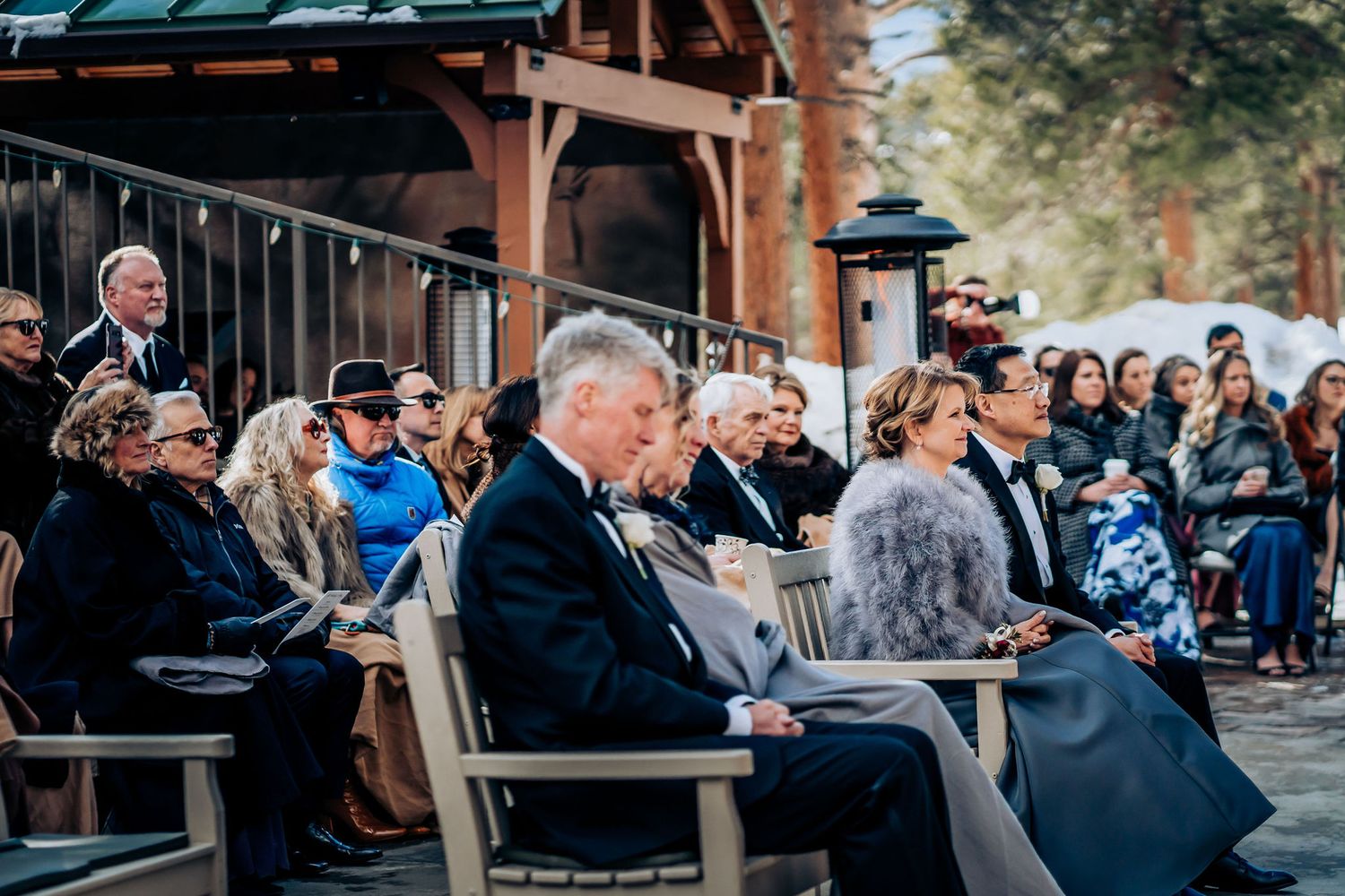 Wedding guests seated outdoors watching ceremony in winter setting.