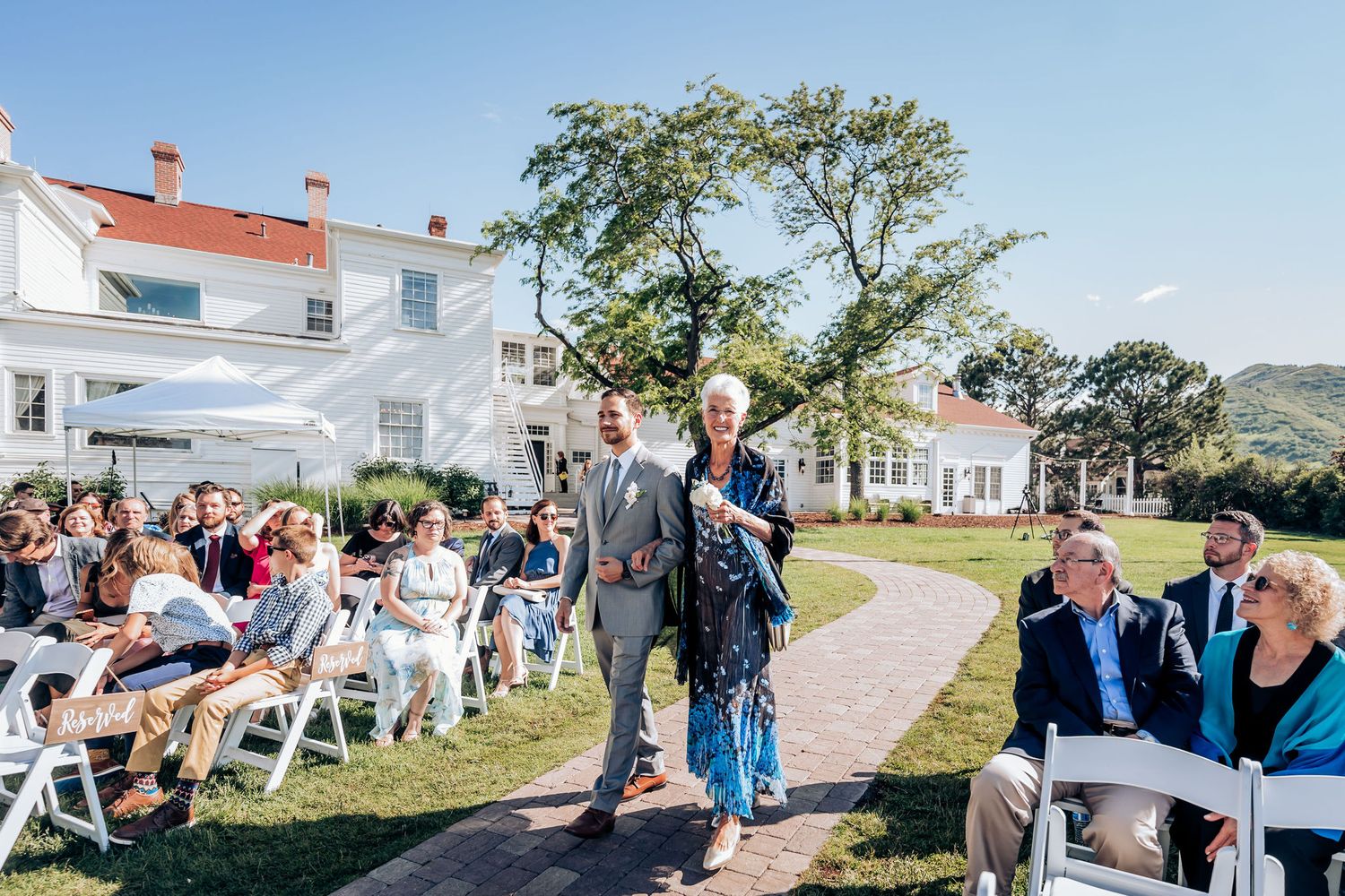 Wedding guests seated in white chairs on lawn in front of historic white mansion.
