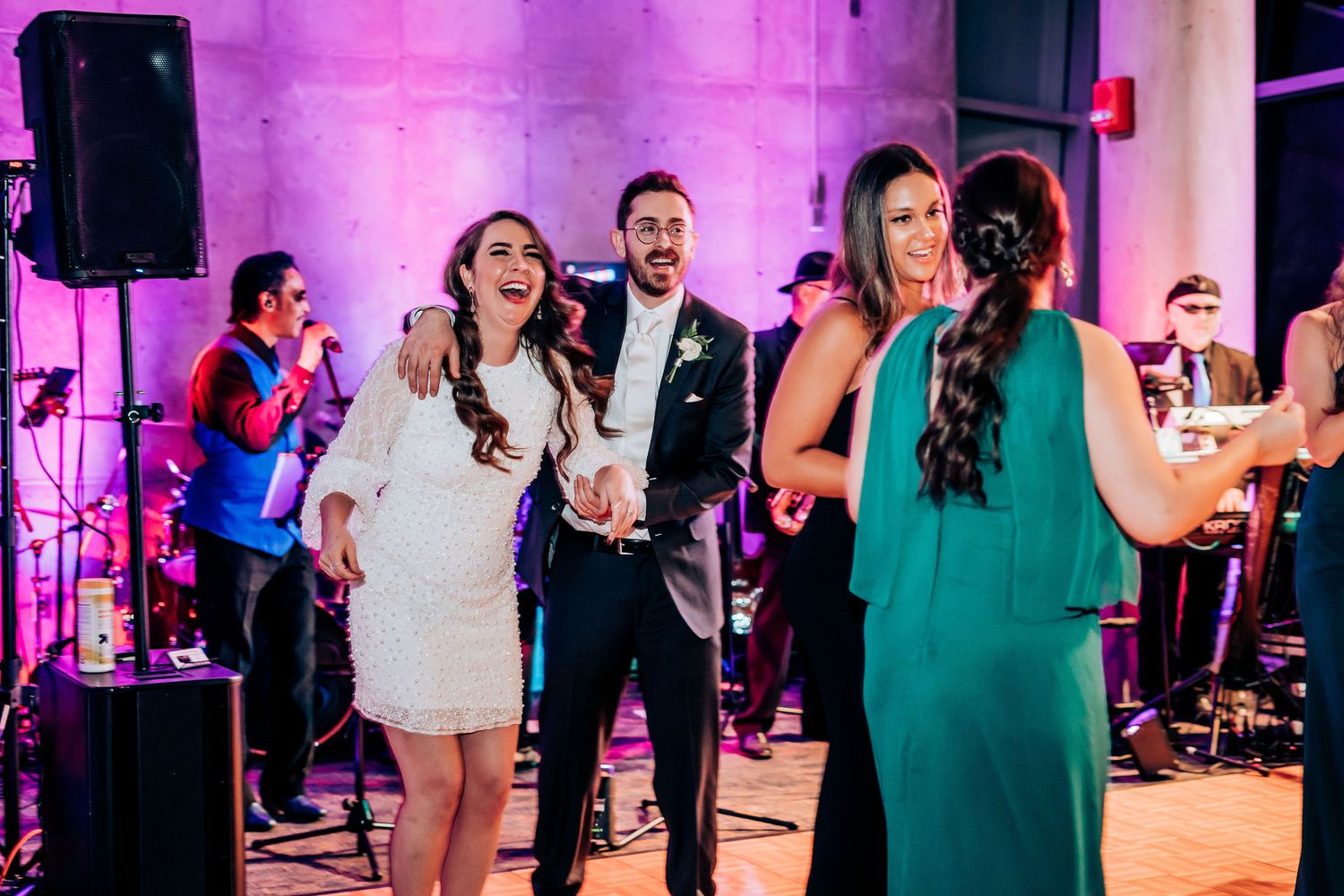 Wedding party dancing and celebrating with live music and purple mood lighting.