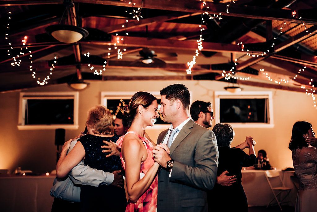 Couples slow dance beneath warm lighting at an intimate indoor wedding reception.