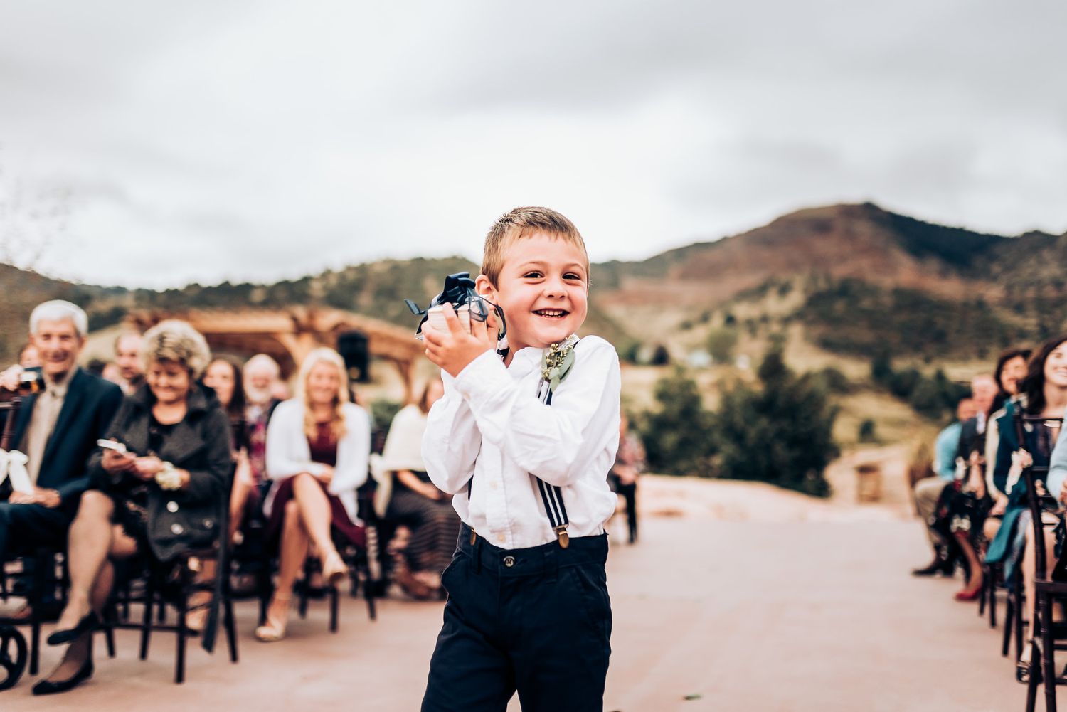 A small ring bearer in white shirt and dark pants walks down the wedding aisle.