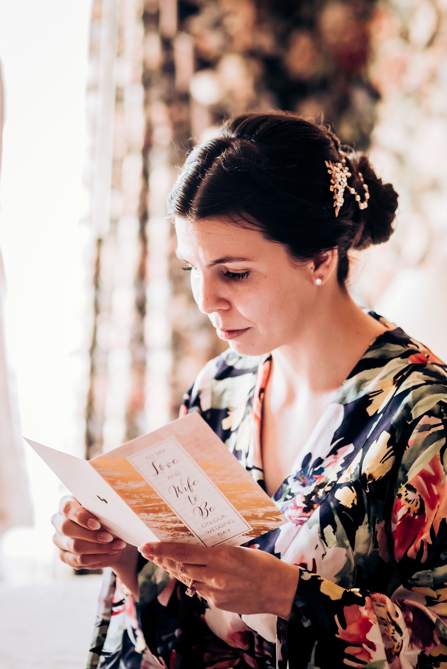 Person in floral print robe reading letter near window.