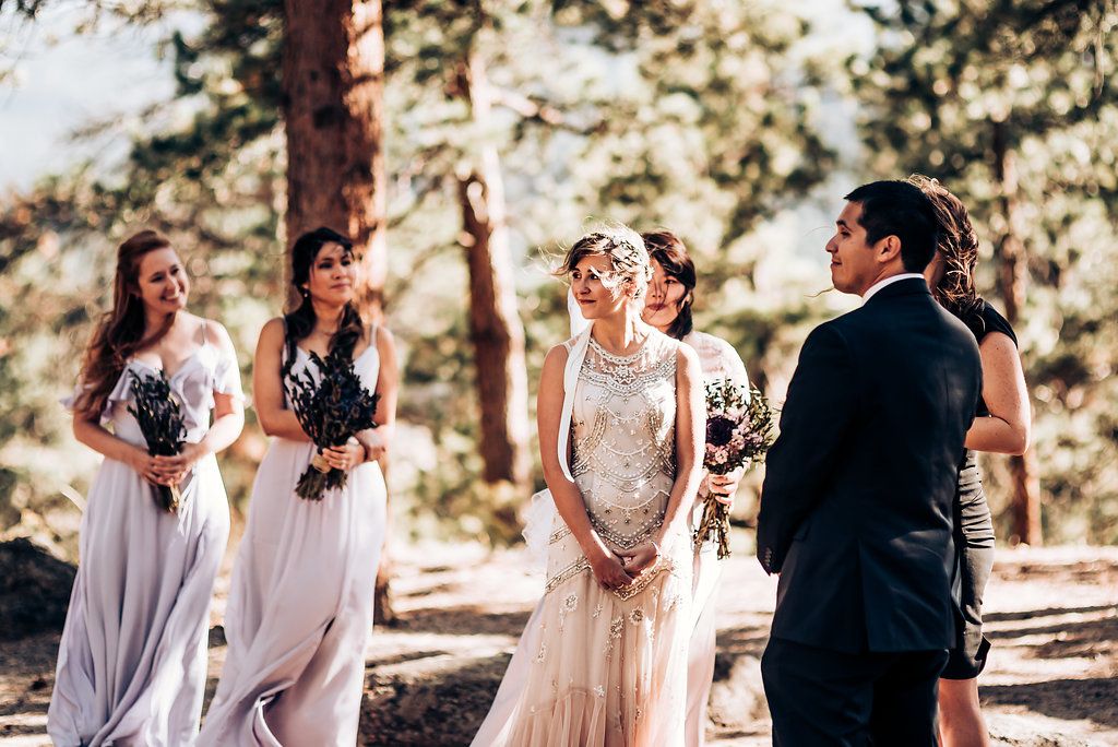 Wedding ceremony participants share joyful moments in a sunlit forest setting.