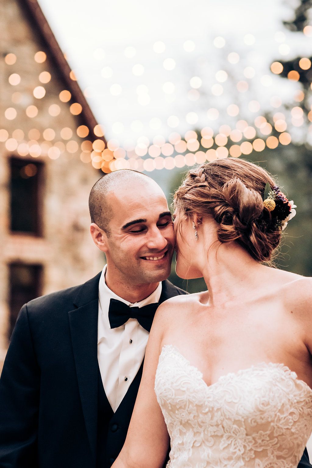 An intimate wedding portrait with twinkling lights and stone architecture in the background.