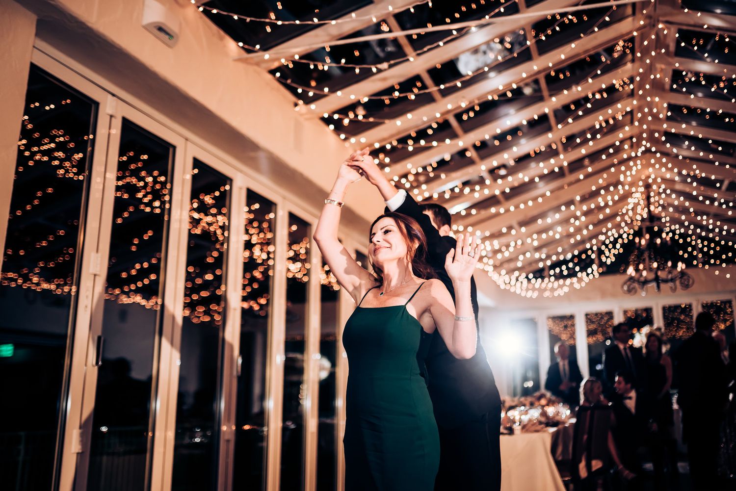 Dancing couple shares an intimate moment under ceiling of twinkling reception lights.