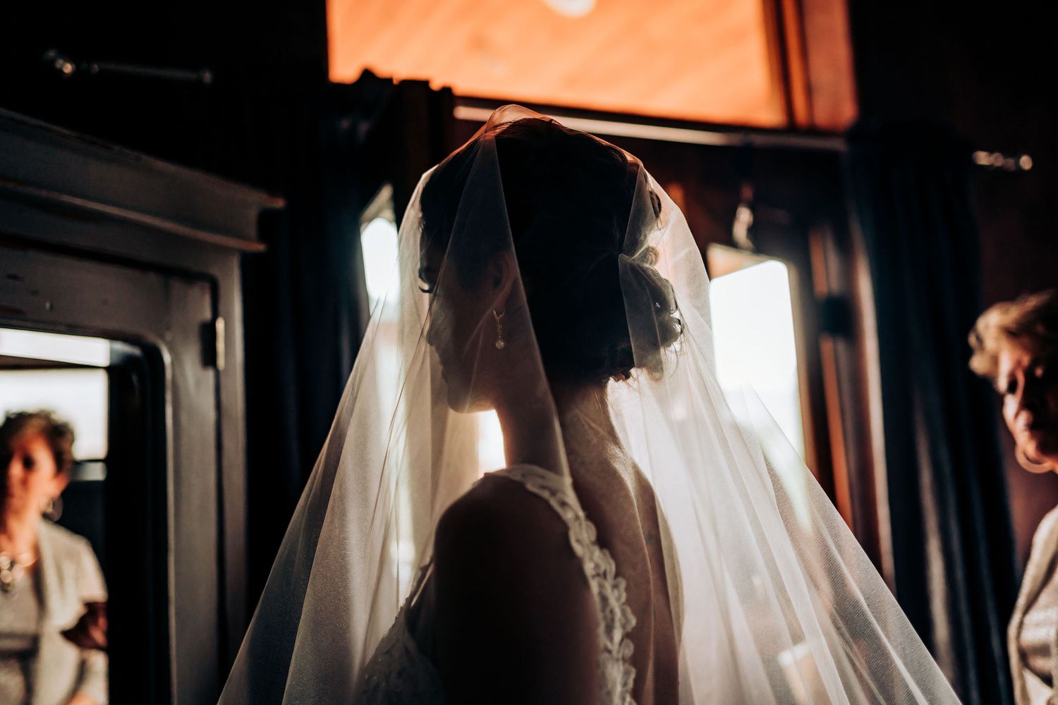 A silhouetted figure in a wedding veil stands in dramatic lighting during wedding preparation.