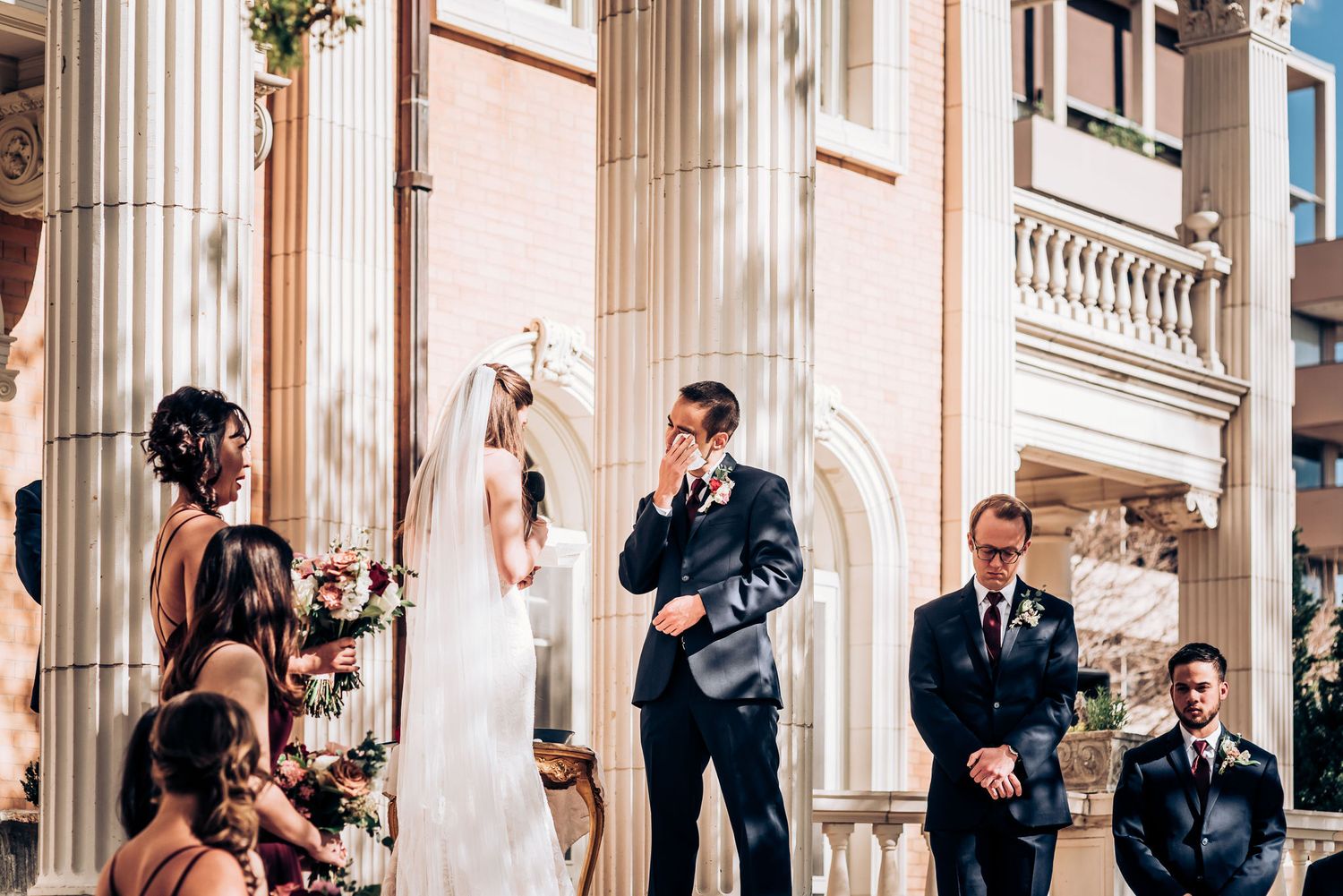 Wedding ceremony on historic building steps with bridesmaids in burgundy dresses.