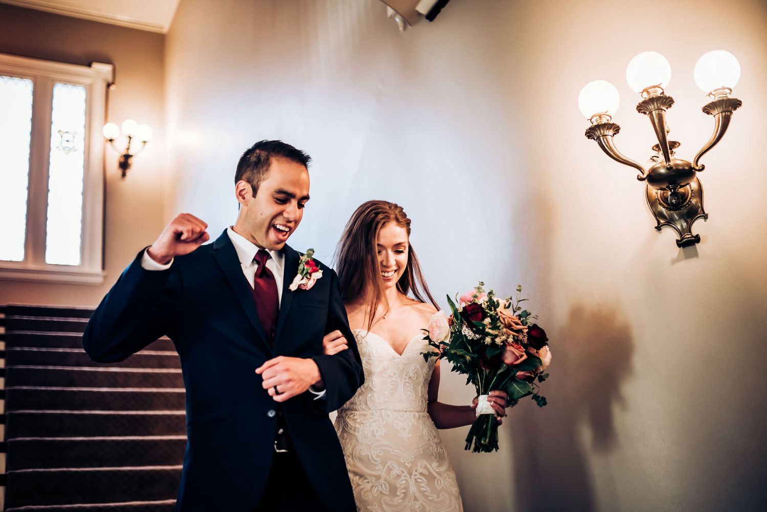 Joyful couple walking down staircase at formal event venue.