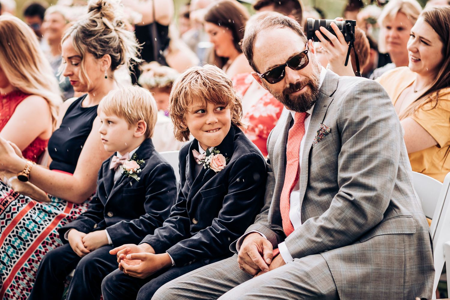 Wedding guests enjoy the outdoor ceremony seating while wearing formal attire.