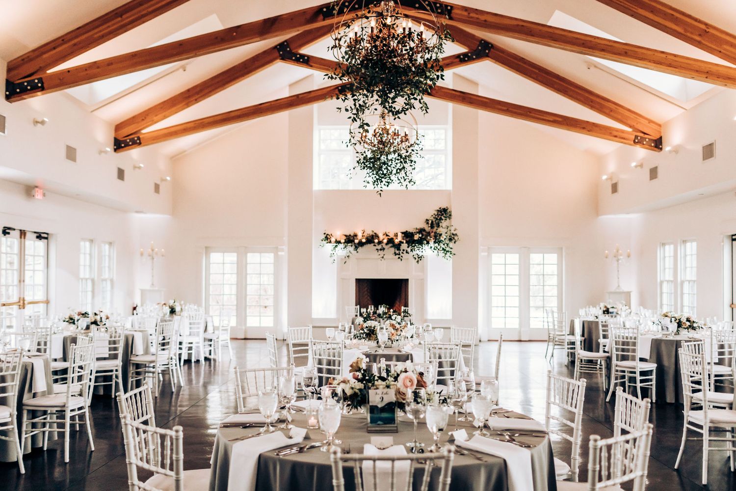 Light-filled wedding reception hall with exposed beams and round tables set for dining.