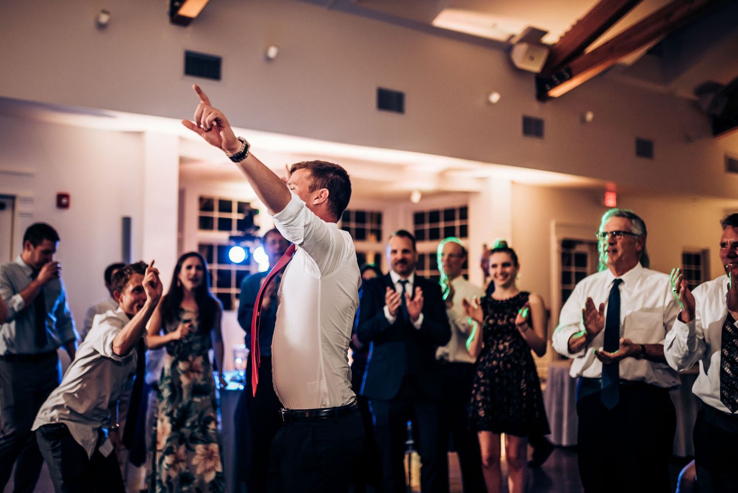 Wedding guest raises a drink in celebration while others cheer during indoor reception.