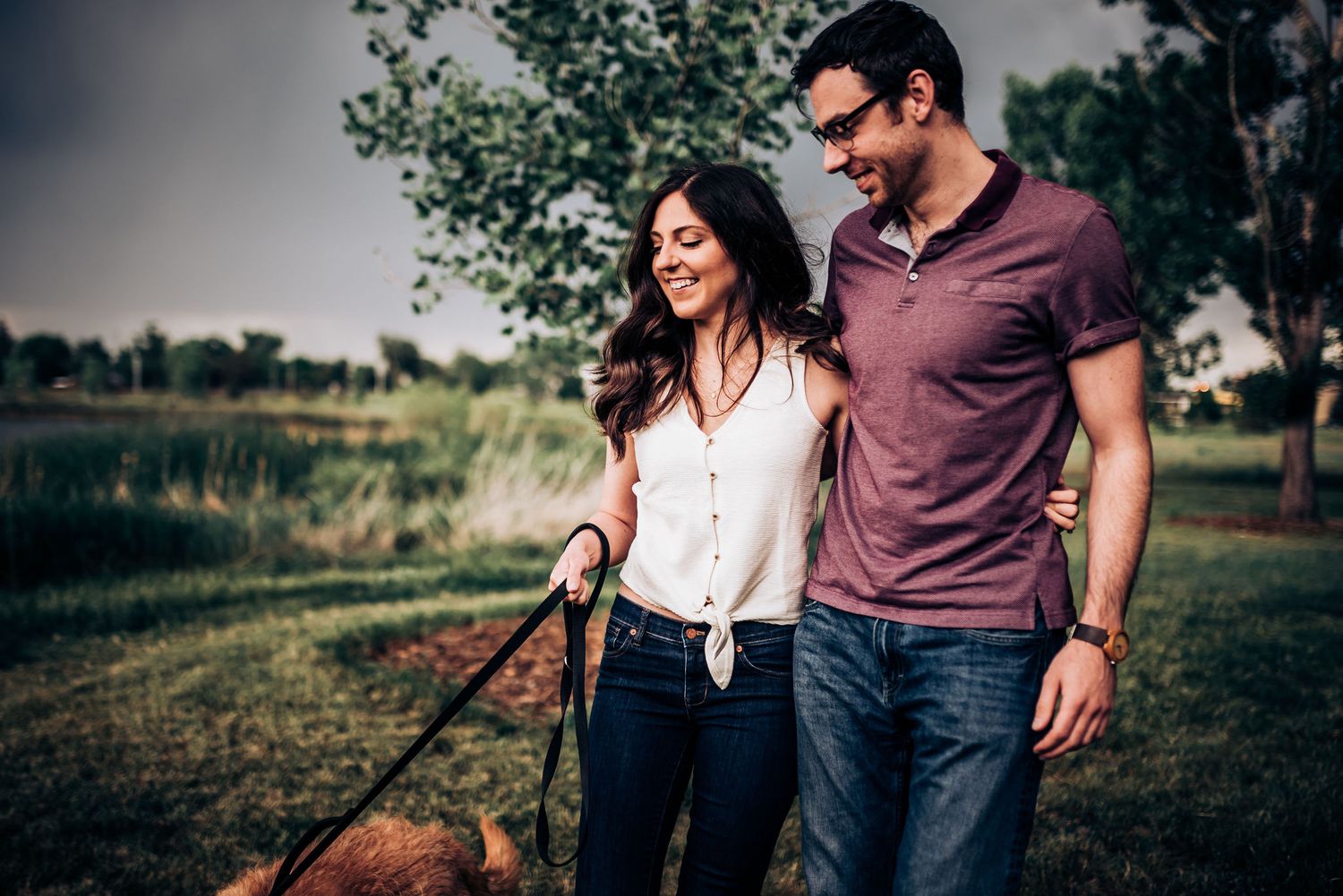 A couple walks together on a casual countryside path during an engagement session.