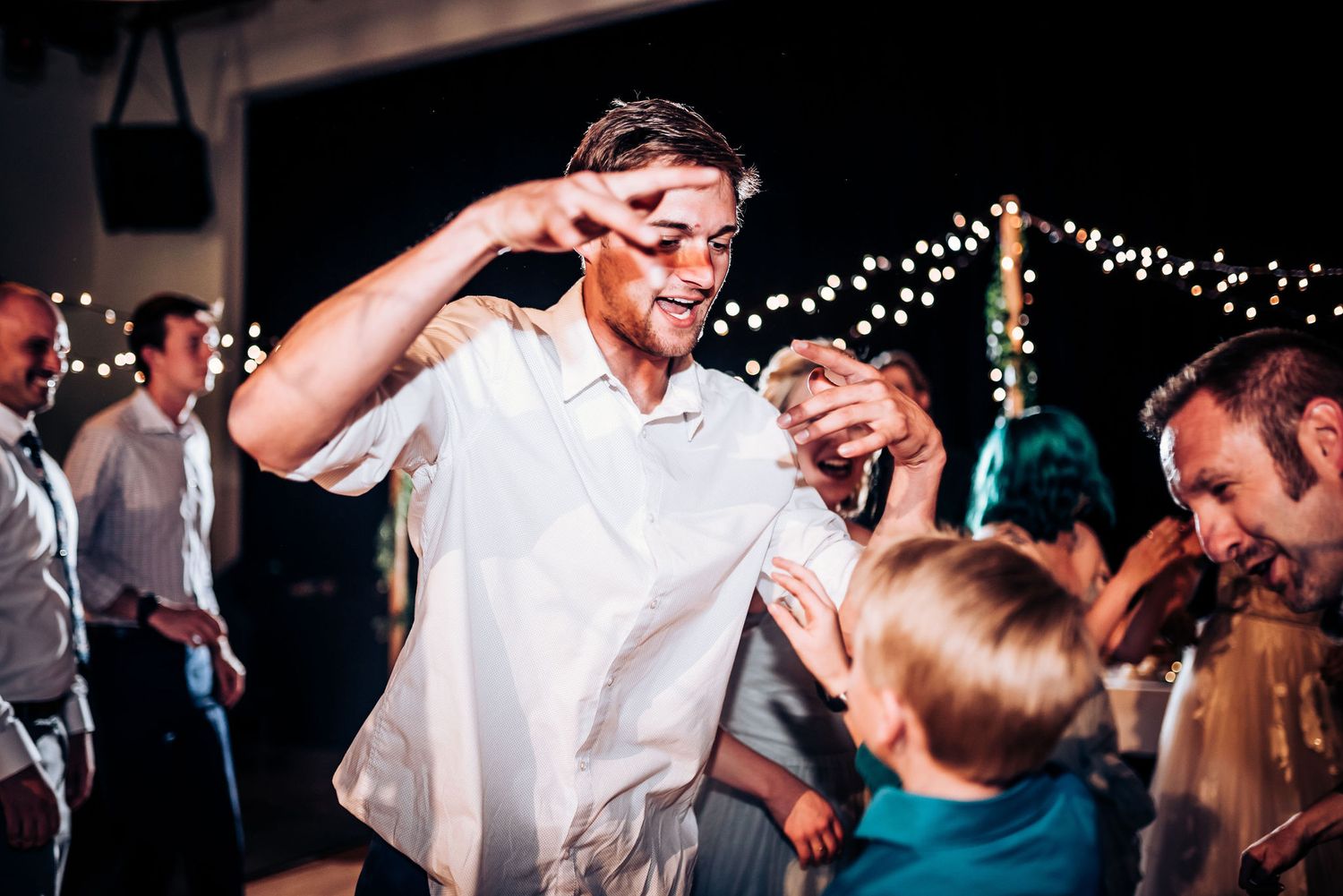 Party guest enjoying lively dance moves at indoor celebration with string light decor.