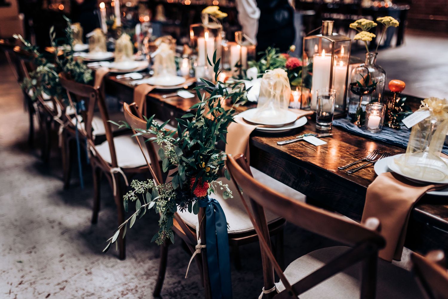 Elegant wedding reception table decorated with greenery garlands and candles in an industrial venue.