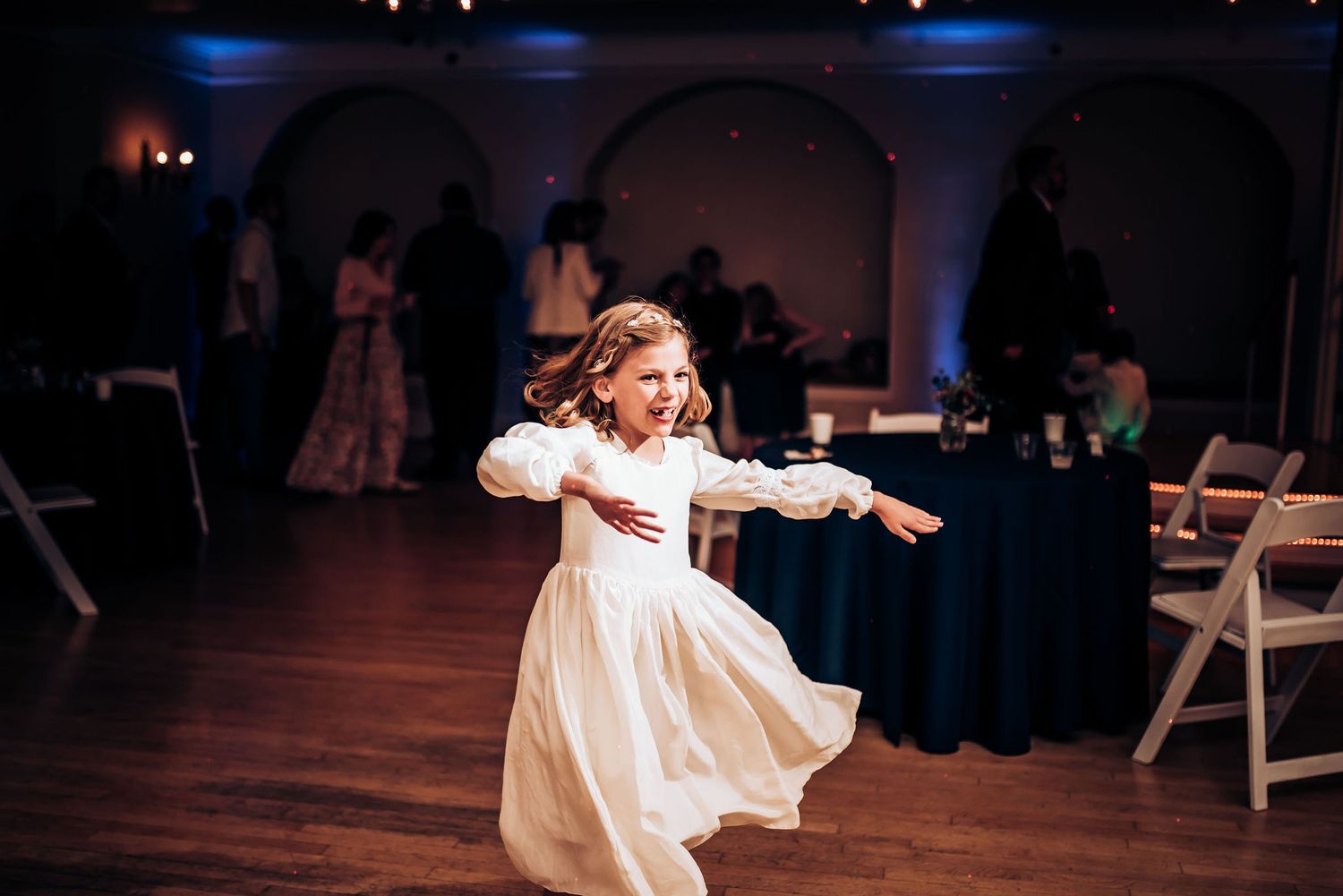 A young dancer in a white dress twirls joyfully on the dance floor.