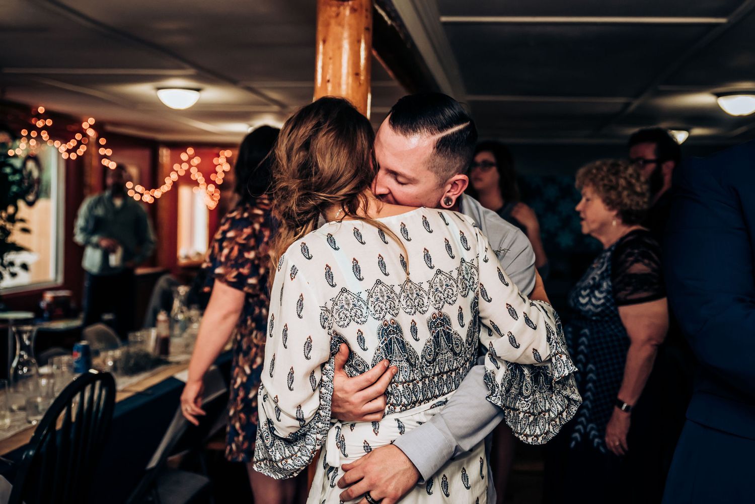 A tender moment shared between two people during a celebration with string lights in background.