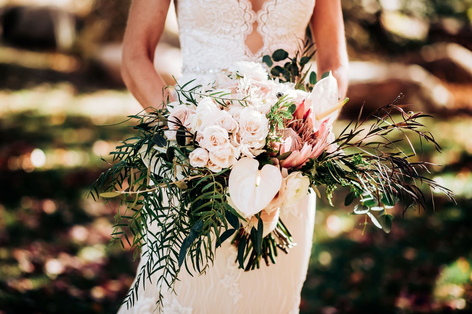 Close-up of bridal bouquet with pink roses, protea flowers and green fern leaves.